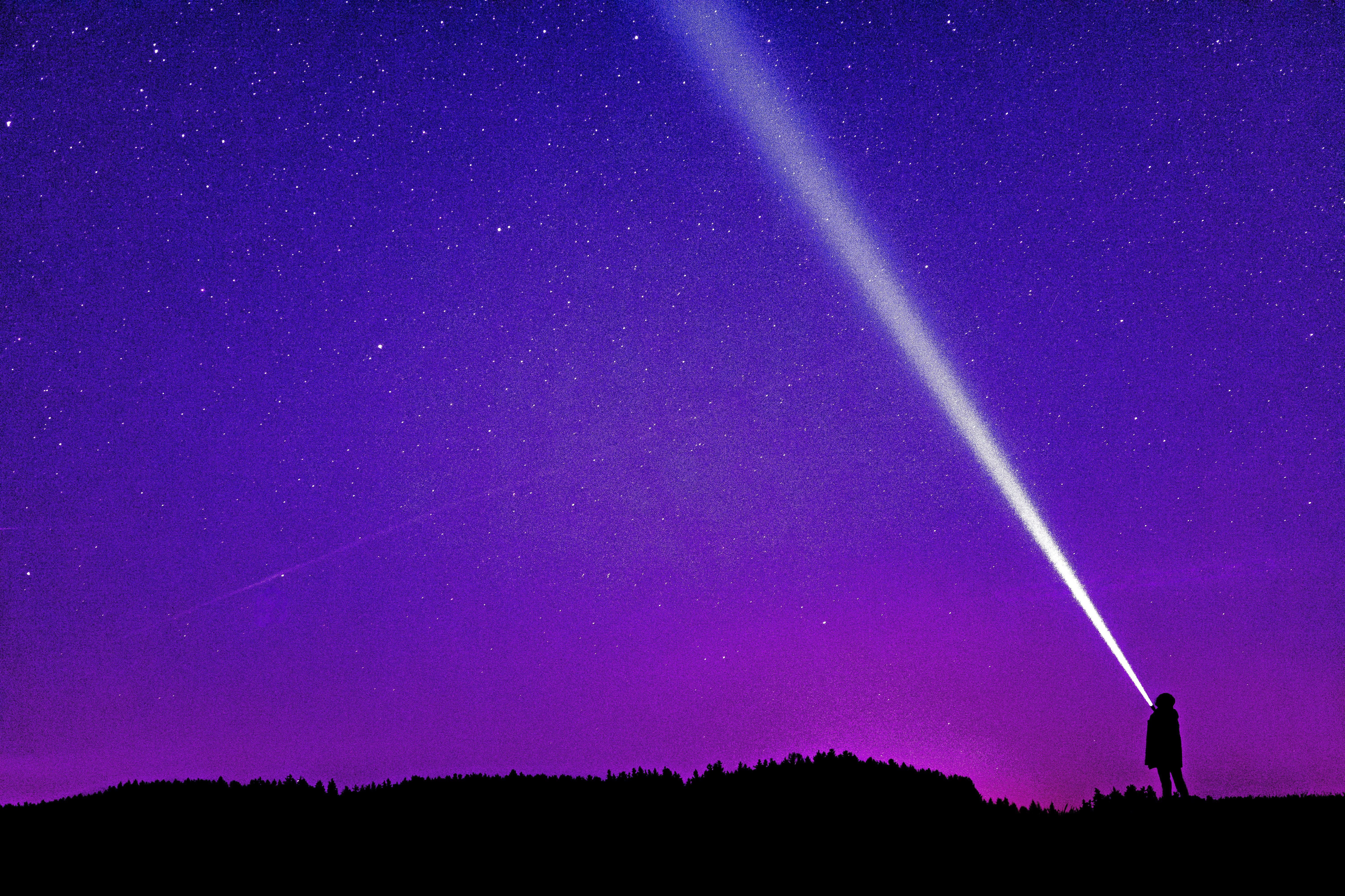 A person pointing a flashlight into the purple night sky